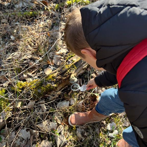 Joris bekijkt met een loep onder de paddenstoel