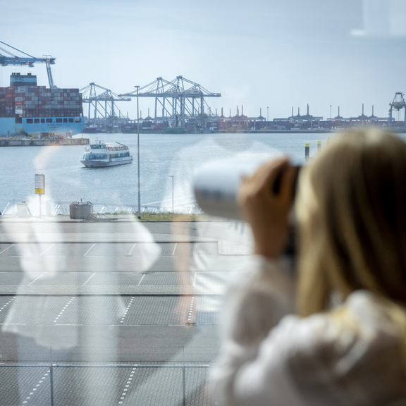 Een bezoeker kijkt door een verrekijker naar de APMT2 Terminals